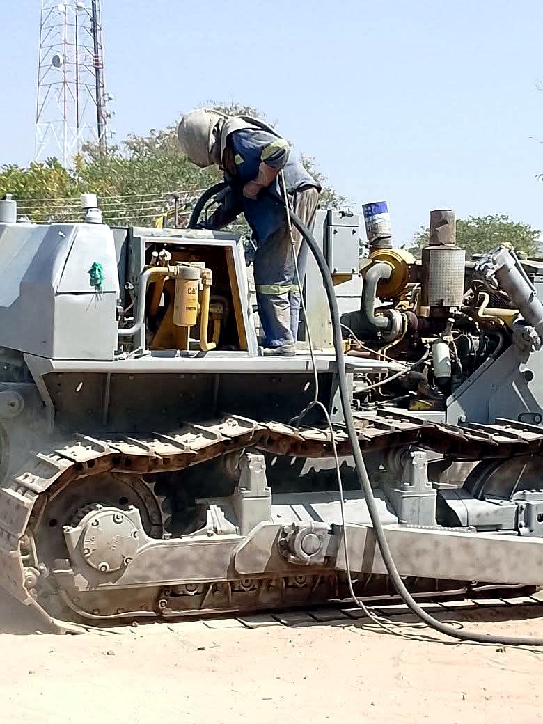 Operator sand blasting a Caterpillar dozer down to bare metal